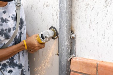 Asyalı işçi genç adam sünger tuğla duvar döşemeye hazırlanmak için çelik bir direkten metal vida kesiyor ve saklıyordu..