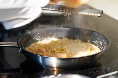 Şef sıcak tavada kremalı spagettiye peynir atar..