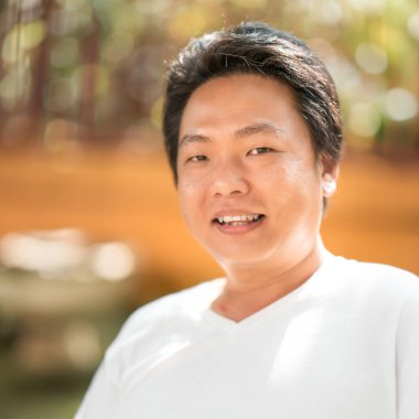 Güneş yüzüne sıcak bir parıltı saçıyor, Asyalı bir adamın dış tarlada çekilmiş vesikalığı, yumuşak, turuncu, kahverengi bir fonda bulanıklaşıyor..