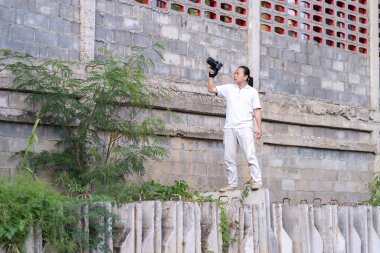 Profesyonel Asya Çincesi - Taylandlı Kameraman duruşu ve görünüm bulucu ve LED ekranda inşaat alanındaki aynasız kamera orta formatında odaklanma.