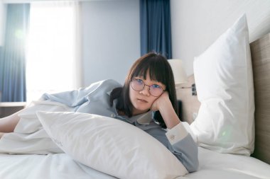 Asyalı genç gözlüklü kadın sabah yatağında yatıyordu..