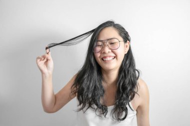 Asyalı utangaç kız mutlu ve saçları stüdyoda açık beyaz arka planda oynarken gülümsüyor.