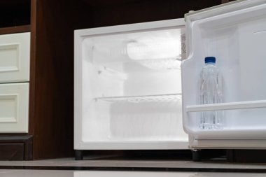 Küçük buzdolabı alçak açılı, boş rafların içinde ahşap tezgahın altında, ahşap dolabın yanında ve lüks bir otel odasında sandalye var.. 