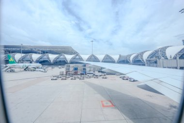 Samut Prakan, Tayland - 9 Temmuz 2023, Suvarnabhumi Uluslararası Havalimanı 'nı ve öğlen saatlerinde uçağın kanatlarını ele geçiren uçağın penceresinden İçeriden Dışarıya Bakış.