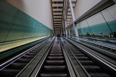 London, England - 10 July 2023, Passengers Stand on the Escalator at Heathrow International Airport, Moving to the Next Floor with Their Belongings. clipart