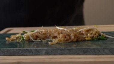 Istakoz Pad Thai, stüdyo ışıklarındaki dikdörtgen tabakta kızarmış erişte, tofu ve diğer malzemelerle servis yapmaya hazır..