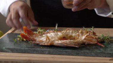 Istakoz Pad Thai, sarı erişte, kızarmış tofu, tere, fasulye filizi, acı biber gücü, sarımsak soğanı ve dikdörtgen bir tabağa konmuş limon ile servis edilir..