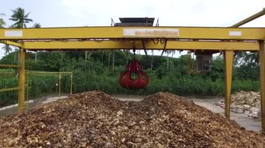 Çimento zemininde kurumuş doğal ham kauçuk yığını ve fabrikanın açık hava bölgesinde mekanik bir yakalayıcı endüstriyel makine var..