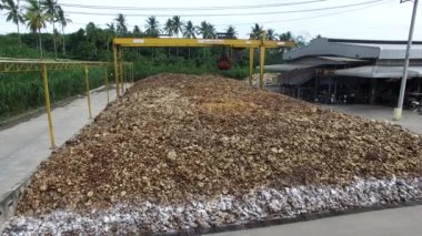 Çimento zemininde kurumuş doğal ham kauçuk yığını ve fabrikanın açık hava bölgesinde mekanik bir yakalayıcı endüstriyel makine var..
