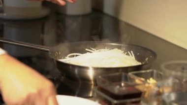 Bir aşçı elektrikli sobada spatulası olan tavada Pad Thai eriştesi kızartır. Geleneksel Pad Thai yemeği için sos tabakları.