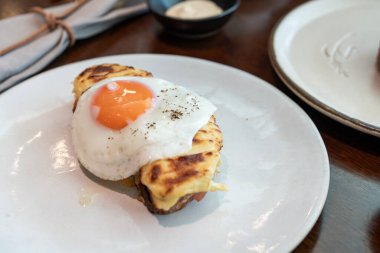 A fried sunny-side-up egg topped with black pepper sits beautifully on melted cheese toast, served on a white plate. Perfect for promoting breakfast menus, cafes, or food blogs. clipart