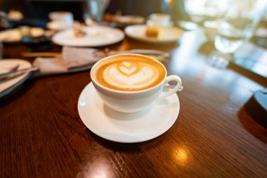 A hot latte with beautiful foam art sits alongside an English breakfast on a rustic wooden table, ideal for showcasing the comfort and charm of cafes and morning dining. clipart