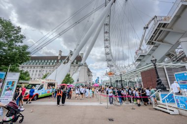 Londra, İngiltere - 10 Temmuz 2023, Londra Gözü 'nün altında sıra bekleyen bir turist kalabalığı, yüksek dönme dolabın arka planında, Londra' nın Güney Şeria 'sını gezen yoğun bir günü yakalıyor..