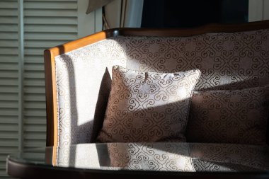 Güneş ışığı, fildişi kadife kumaş ve oturma odasındaki yuvarlak kahve masasıyla döşenmiş zarif ahşap koltukta parlıyor..