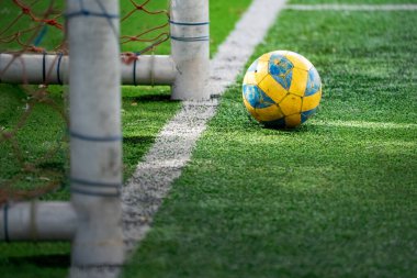 yellow football or soccer ball lying on the artificial grass with little sun ray coming through of it.