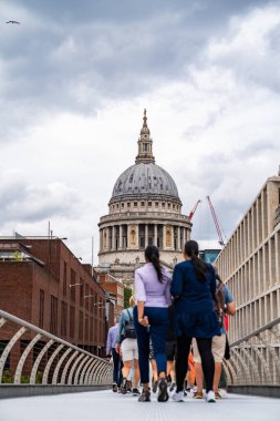Millennium Köprüsü 'nden St. Pauls Katedrali' nin manzarası canlı, insanlar ona doğru yürüyor, modern hareketi tarihi mimariyle harmanlıyor..