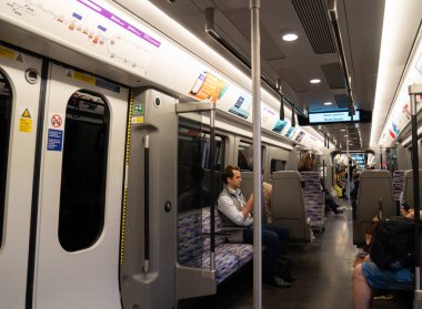Londra, İngiltere, 11 Temmuz 2023, Yolcular imzalı bir Elizabeth Line trenine biniyor Mor koltuklar ve Modern İçişleriyle çevrili.