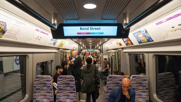 Londra, İngiltere, 11 Temmuz 2023, Yolcular imzalı bir Elizabeth Line trenine biniyor Mor koltuklar ve Modern İçişleriyle çevrili.