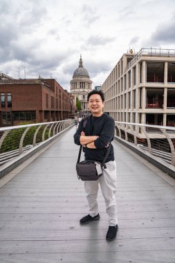 Milenyum Köprüsü 'ndeki Asyalı bir turist St. Pauls Katedrali' ne bakıyor ve Londra 'nın ikonik siluetine bir bakış açısı sunuyor..