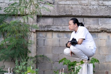 Asyalı profesyonel kameraman oturur ve inşaat alanında ve çevrede nasıl yaratıcılık fotoğrafı oluşturulacağını düşünür..