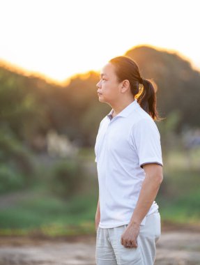 Asyalı uzun saçlı adam altın alacakaranlıkta kuru tarlada duruyor ve dinleniyor..