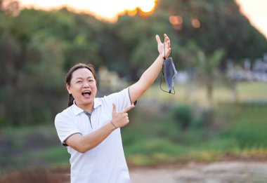 Asyalı adam maskesini çıkar ve altın alacakaranlıkta elini kaldır.