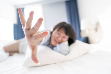 Soyut ve bulanık Asyalı tatlı kadın beyaz yastığa ve yatağa uzanıyor sonra elini kameraya kaldırıyor..