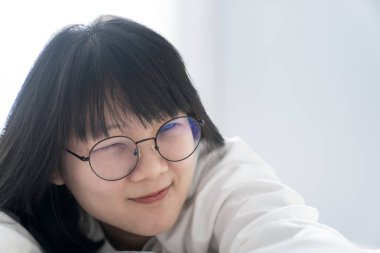 Kırpılmış gözlük tatlı, tatlı Asyalı kız mutlu ve rahat bir şekilde yatar sabah pencerenin önünde..