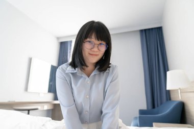 Asyalı gözlüklü, mavi gömlekli, yatak odasındaki pencere lambasının yanında hoş bir kadın..