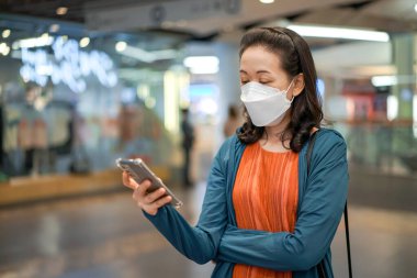 Asyalı Taylandlı kadın maske takıyor ve bir mağazada veya bakkalda cep telefonu çalıyor.
