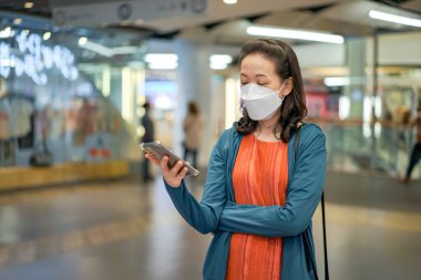 Asyalı Taylandlı kadın maske takıyor ve bir mağazada veya bakkalda cep telefonu çalıyor.
