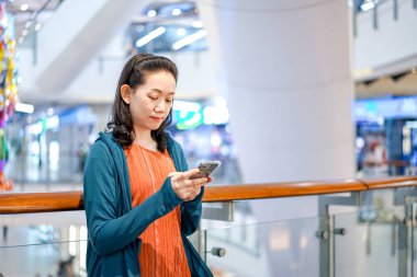 Güzel Asyalı Kadın, Bangkok 'taki mağaza atmosferinde cep telefonu tutuyor ve oynuyor.
