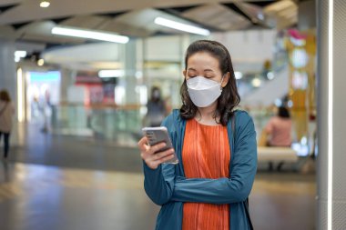 Asyalı Taylandlı kadın maske takıyor ve bir mağazada veya bakkalda cep telefonu çalıyor.