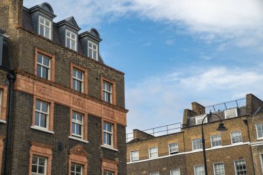 Geleneksel Teraslı evler Yeşil Ağaçlı Sessiz bir cadde ve Kırmızı Londra Otobüsü Mahallenin Sakin Atmosferini Yansıtıyor.