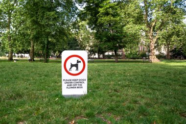 Köpekleri kontrol etmek ve çiçek tarlalarından uzak tutmak için bir parkta imza atın. Yeşil çimen ağaçları ve kamusal alanla çevrili.