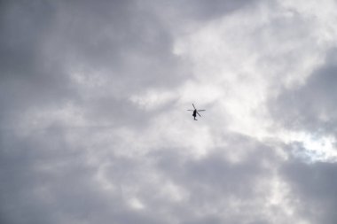 Bir helikopter, başkası yok. Gökyüzü kalın ve sessiz. Çizgiler basit kalır. Hareket içindeki karanlık, grinin altındaki mesafeyi, niyeti ya da tetikte olmayı önerir..
