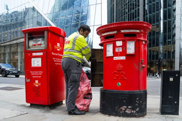 Londra, İngiltere, 11 Temmuz 2023, Modern Ofis Binaları Tarafından Çerçevelenen Geleneksel Kırmızı Posta Kutusundan Posta Topluyor..