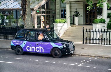 Londra, İngiltere, 12 Temmuz 2023, Canlı Mor Reklamlı Klasik Siyah Londra Taksisi Bir Yolcu Bırakılırken Bir Otel Girişine Park Edildi