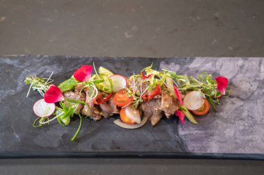 Üzerine tereyle süslenmiş baharatlı Tayland bifteği salatası ve mikro bitkiler dikdörtgen taştan bir tabağa konuldu..