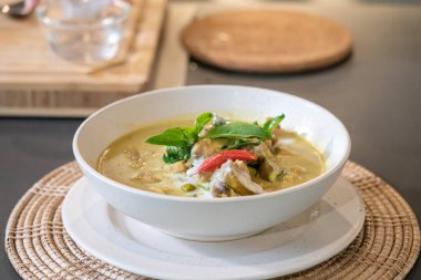 Üzerine biber ve fesleğen ile süslenmiş yeşil körili tavuk hasır krem rengi plasemat ile servis edildi..