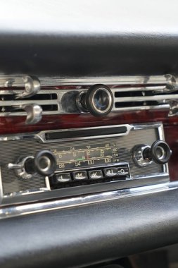 Klasik bir arabanın gösterge panelinde ayrıntılı analog göstergeler, bir radyo ve cilalanmış ahşap ve krom havalandırma delikleri var..