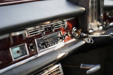 Klasik bir arabanın gösterge panelinde ayrıntılı analog göstergeler, bir radyo ve cilalanmış ahşap ve krom havalandırma delikleri var..