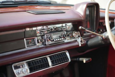 Klasik bir arabanın gösterge panelinde ayrıntılı analog göstergeler, bir radyo ve cilalanmış ahşap ve krom havalandırma delikleri var..