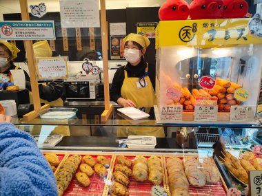 Kamakura, Japonya, 14 Mar 2024, Sokak Gıda Dükkanı çeşitli Japon kızartmaları satıyor ve tezgahta müşterilere servis yapan sarı üniformalı personel var..