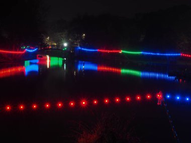 Sükunet içindeki Peasholm Parkı 'nın üzerindeki köprü, Scarborough, geceleyin, suya yansıyan kırmızı, yeşil ve mavi ışıklarla, Kuzey Yorkshire, İngiltere