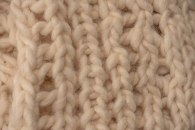A fragment of beige knitted fabric, knitted from white sheep wool. Knitted background. 
