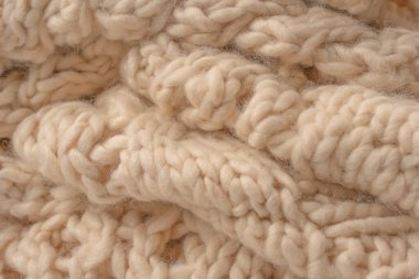 A fragment of beige knitted fabric, knitted from white sheep wool. Knitted background. 