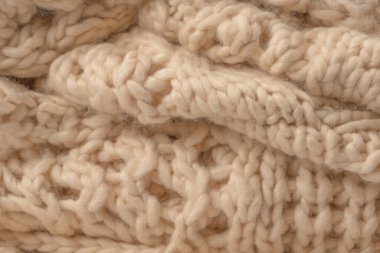 A fragment of beige knitted fabric, knitted from white sheep wool. Knitted background. 