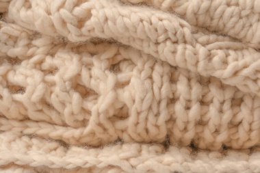 A fragment of beige knitted fabric, knitted from white sheep wool. Knitted background. 