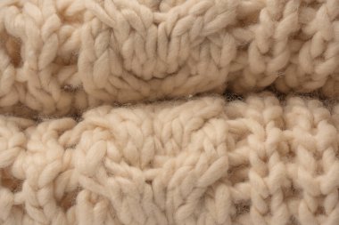 A fragment of beige knitted fabric, knitted from white sheep wool. Knitted background. 